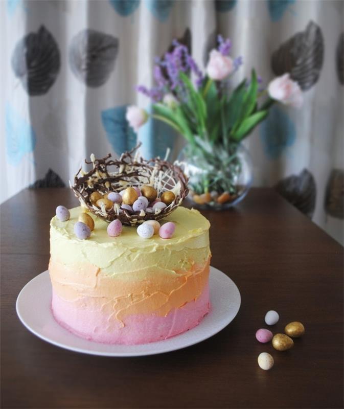 torta iz velikonočnega gnezda s prelivom iz rožnate, oranžne in rumene maslene kreme z gnezdom iz temne in bele čokolade