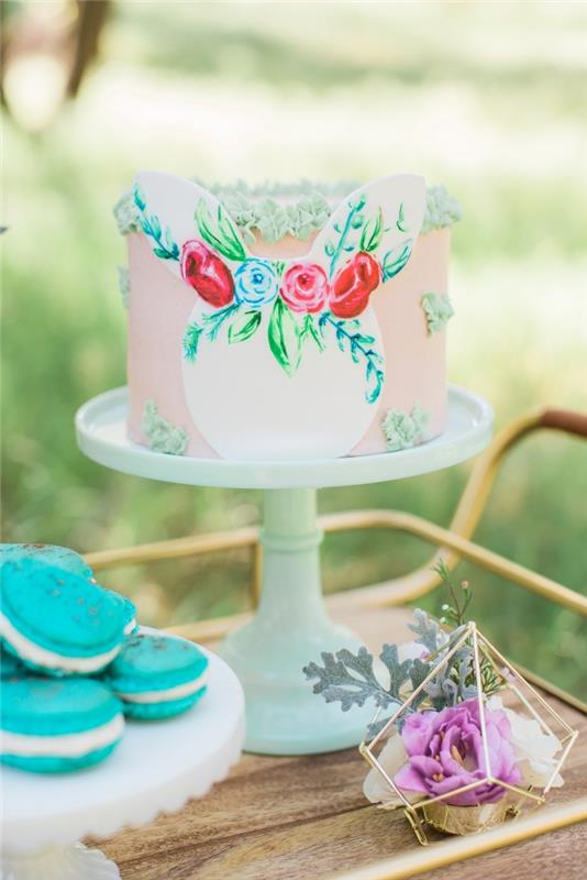 lepa plast torte z gladko rožnato glazuro, okrašeno z majhnimi cvetovi, narejenimi iz slaščičarske vrečke in papirnate zajčje glave