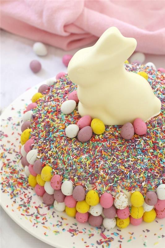 enostavna in hitra velikonočna torta, okrašena z večbarvnimi sladkornimi posipi, majhnimi čokoladnimi jajci in zajčkom iz bele čokolade