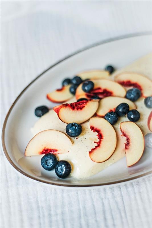 lengvas ir gaivus vasaros desertas iš vanilinės panna cotta, papuoštas persikais ir mėlynėmis