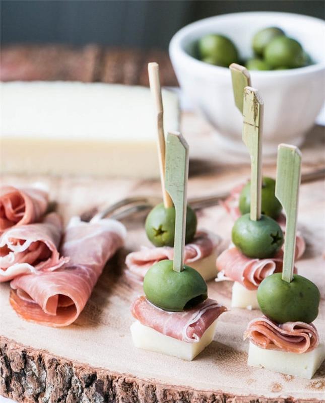 idėja apie paprastą apero iešmą, pagamintą iš manchego sūrio, alyvuogių ir prosciutto, patiekto ant medinio rąsto, valgis su draugais