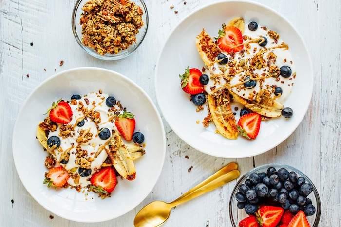 bananas, braškės, mėlynės su graikišku jogurtu ir granola, museli, sveikos ir spalvingos pusryčių lėkštės idėja