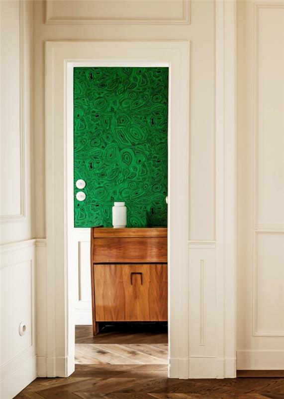 senovinės išvaizdos miegamojo durys, padengtos malachito žalios spalvos tapetais, puikiai derančios su senovine medine spintele ir balto medžio sienų dailylentėmis