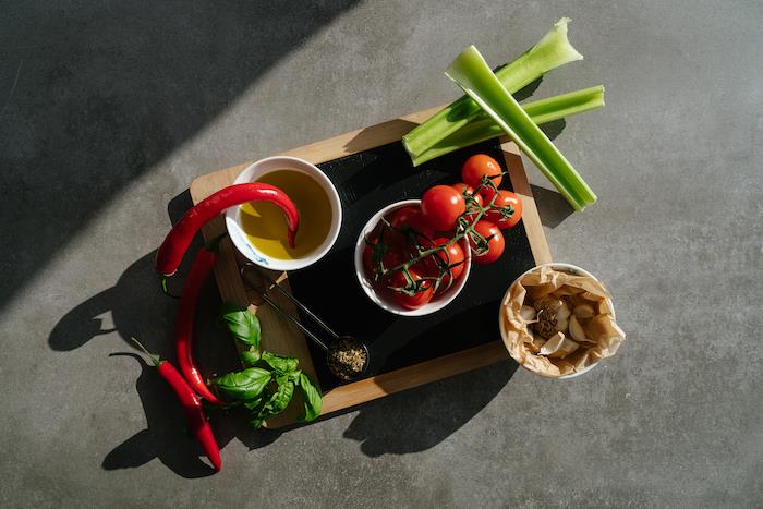 ahşap kesme tahtası, domates çorbası, gri tezgah üzerinde düzenlenmiş biber ve domates, kereviz ve sarımsak