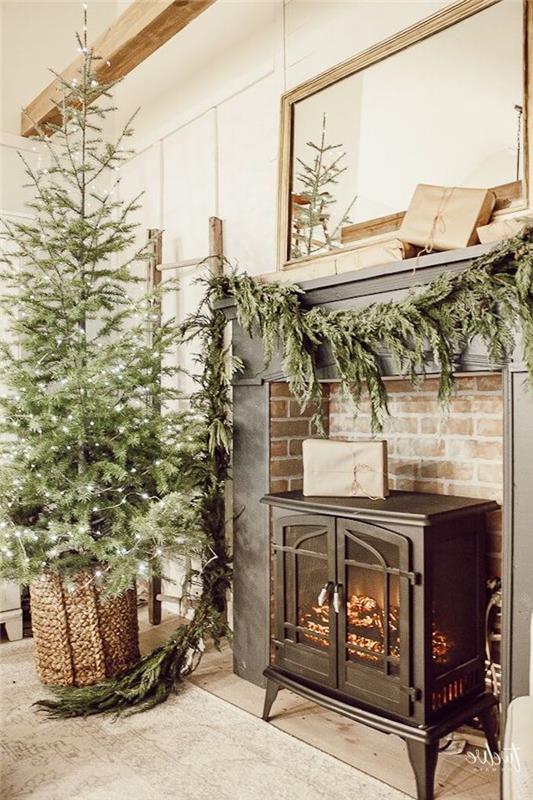 Çekmeceli bir Noel şöminesi, yanında bir ağaç ve yeşilliklerde asılı çelenkler