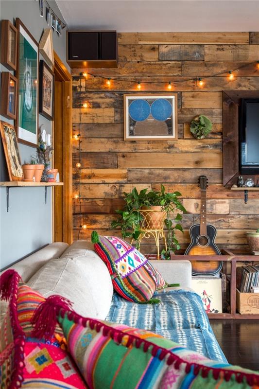 šiltas kaimiško ir prašmatnaus bohemiško stiliaus svetainės dekoras su mediniais baldais ir spalvingomis pagalvėmis su etniniais motyvais