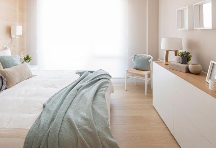 Yatak odasında hafif ahşap duvarlar ve pastel yeşil minderler ve örtüler ile zemin ile İskandinav ve minimalist ruh