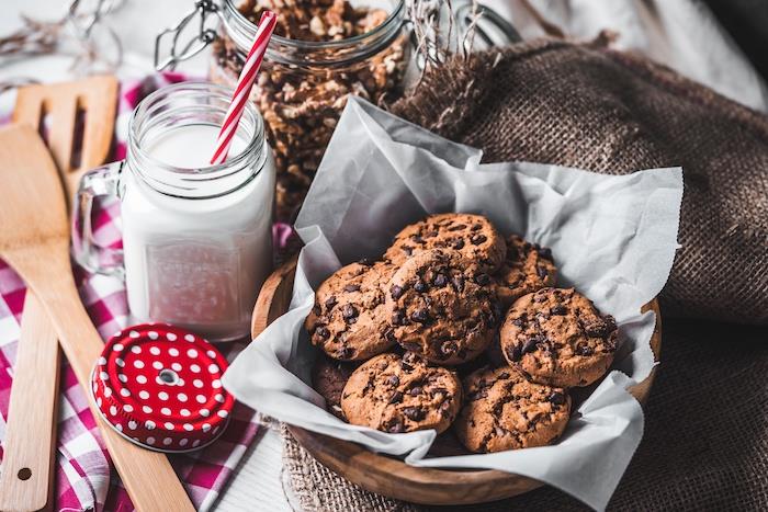 Ciotola di legno, piatto con piškotki, biscotto al cioccolato, barattolo di vetro con latte