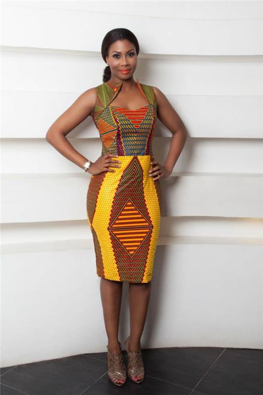 Afriška moda, afriška obleka brez rokavov, dragi izrez, pod kolenskim krilom v rumeni in rjavi barvi, sandale s čipkami v svetlo rjavi barvi
