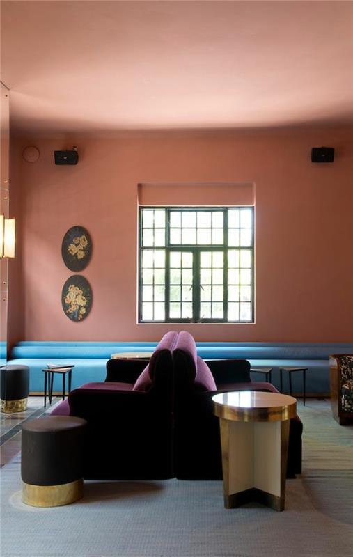 koralno roza stena, lila zofe, velik modri kavč, okno, preprosta in elegantna notranjost