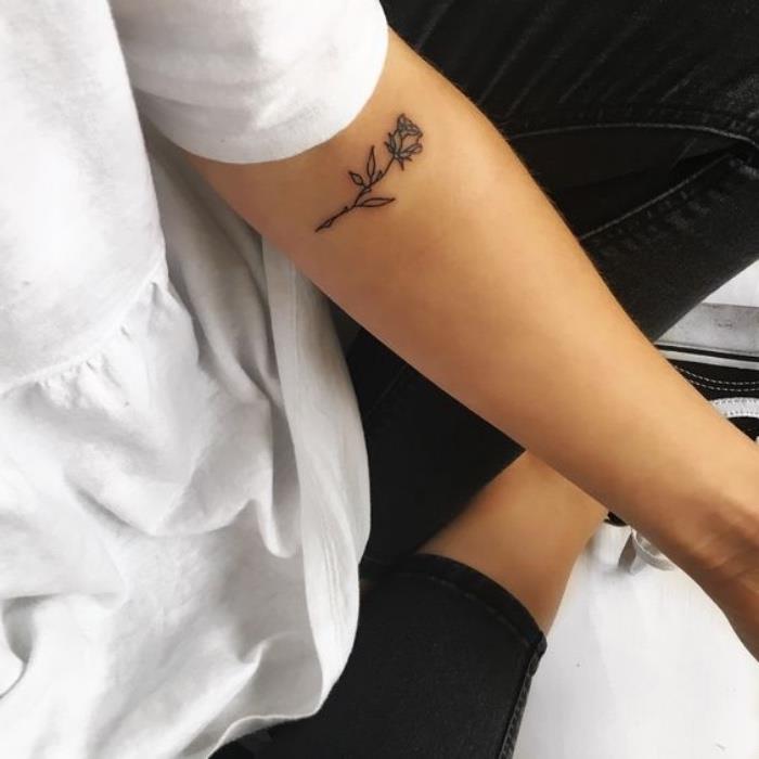 mažos rožės dilbio tatuiruotė, maža saulėgrąžų tatuiruotė, moteris dėvi baltą palaidinę, juodos kelnės