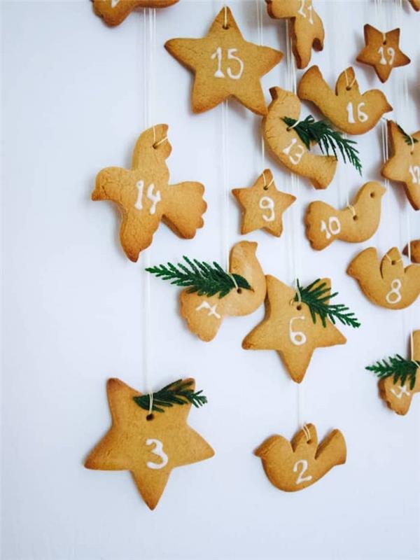sunumeruoti kalėdiniai sausainiai su baltu numeriu ir pušies šakelių puošmena, kabanti ant balto siūlo, suasmenintas gurmanų advento kalendorius