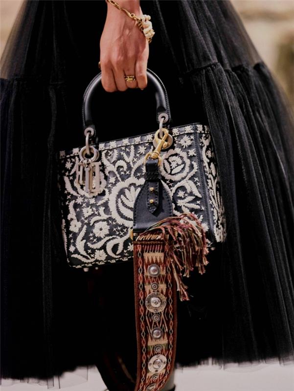 ilgas juodas sijonas, tekstūruotas krepšys su gėlių figūromis, auksinė apyrankė, juoda pareiškimo rankena