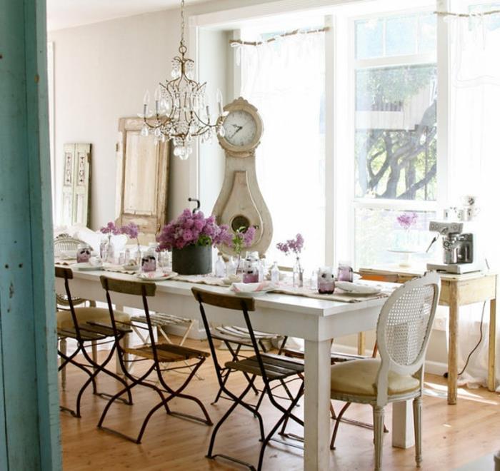 ideja za jedilnico country chic, miza iz belega lesa, stol iz lesa in kovine, ura, eleganten lestenec, lahek parket, cvetlični osrednji del