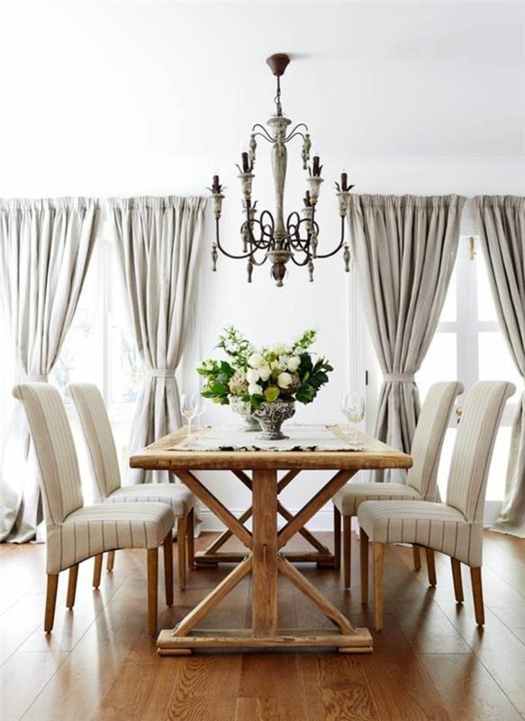 ideja, kako okrasiti jedilnico, svetel parket, elegantno podeželsko mizo, bele stole, baročni lestenec, sive zavese, cvetlični osrednji del