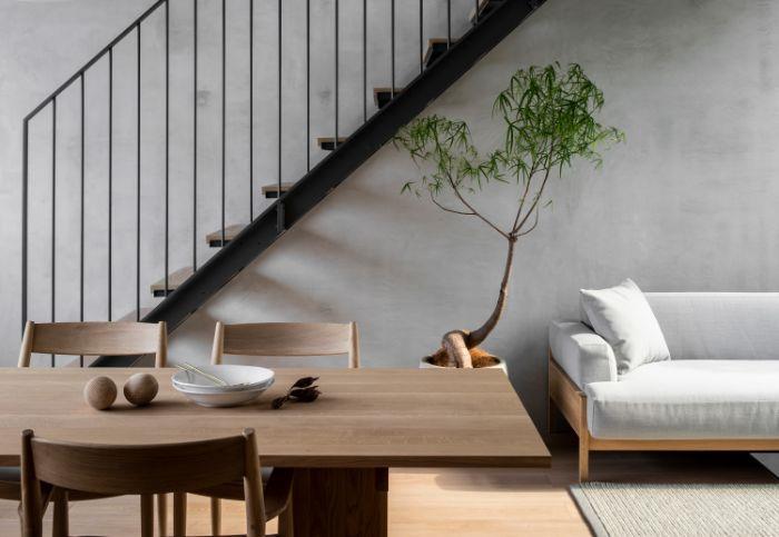 Stol za jedilnico in lesena miza odprta za minimalistično dnevno sobo v lesenem kavču z belo blazino siva stena zelena rastlina lahki lesen parket