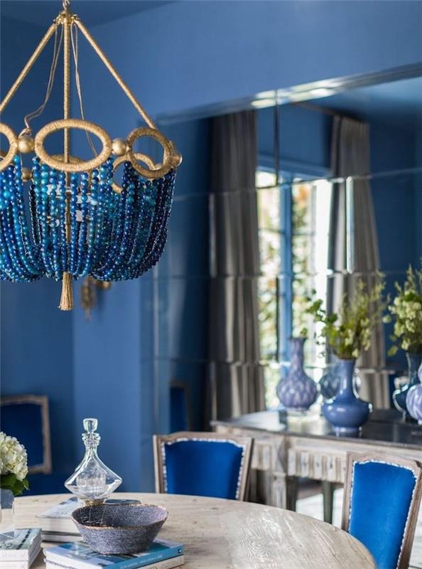 sodoben model jedilnice z modrimi stenami, jedilna miza iz surovega lesa, modri stoli, vaza z zelenimi vejami