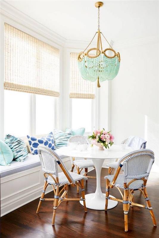 baltas valgomasis, baltas stalas ir medinės kėdės bei baltas sofos audinys, mėtos žalios pagalvėlės ir liustra, gėlių puokštė