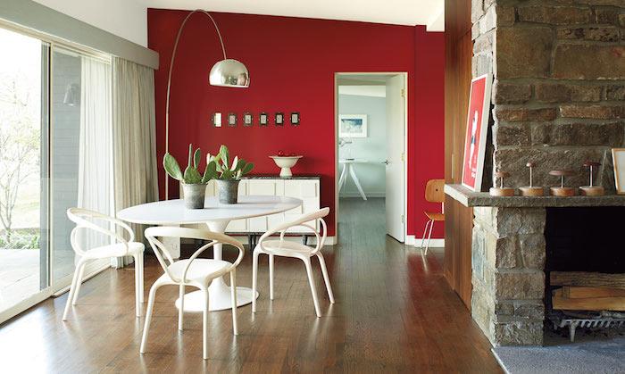 sodobna jedilnica z belo oblikovalsko mizo in stoli na temnih lesenih tleh in rdeči steni