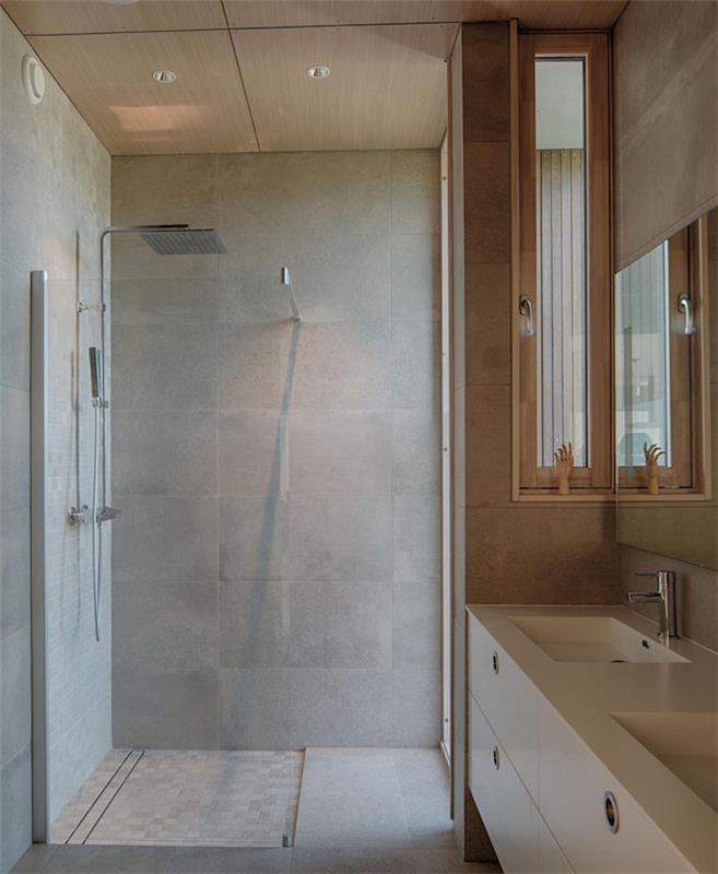 kopalnica iz sivih voščenih betonskih ploščic s kabino za prhanje in kvadratne bele omare za umivalnik v švedskem slogu