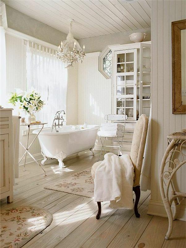 vonios kambarys su šviesiomis medinėmis grindimis ir balta vonia su krištolo liustra