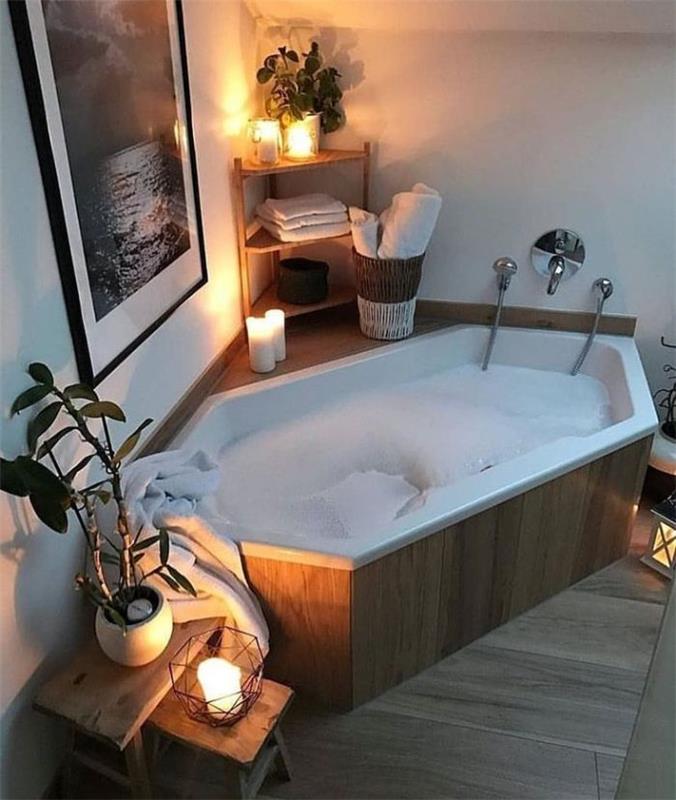 medinis ir baltas vonios kambarys su minkšta šviesa, žvakėmis, žaliais augalais ir medine vonia