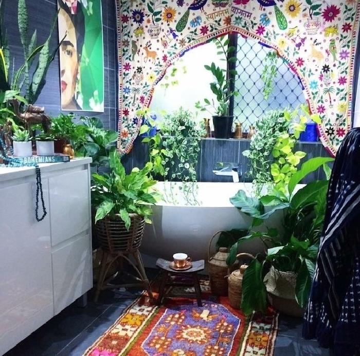 stenski okvir dece frida khalo, orientalska preproga na tleh s sivimi ploščicami, bela kopalniška omara, več rastlin okoli kadi, orientalsko potiskana tekstilna plošča