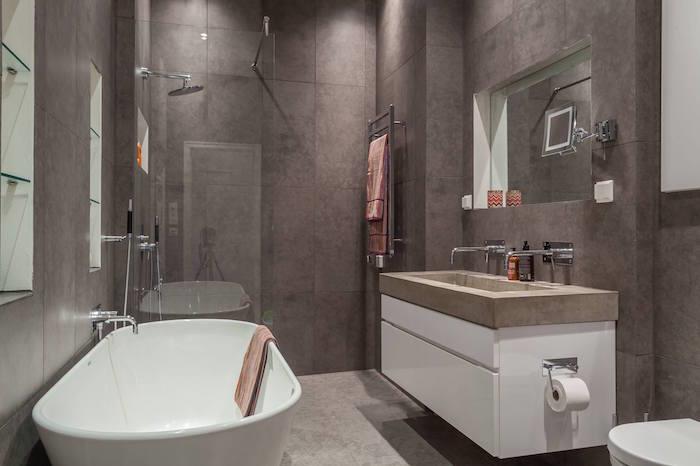 majhna siva kopalnica, prekrita s ploščicami na stenah in poliranim betonskim podom s tuš kabino in umivalnikom cementa v skandinavskem slogu
