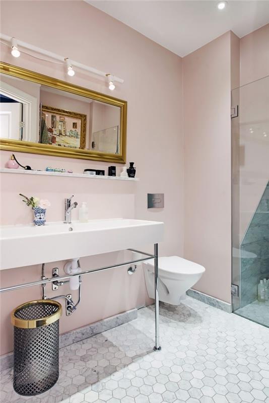 vonios kambario apdaila su šviesiai rožinėmis sienomis ir baltomis lubomis, stačiakampio aukso veidrodžio modelis su pramoniniu apšvietimu