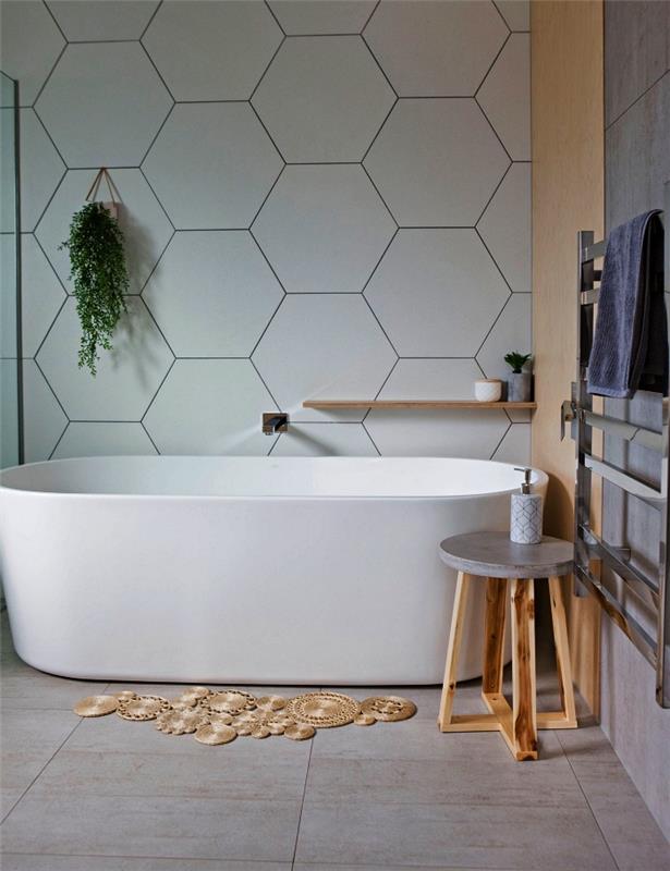 bela kopalnica s sodobno ovalno kadjo ob steni v šesterokotni stenski plošči z vzorcem, naravni dekor z boemsko preprogo iz rastlinskih vlaken in stransko mizo iz lesa in betona