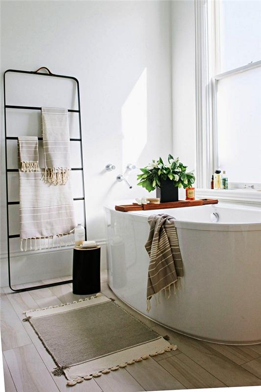 dekoracija kopalnice v naravi z ovalno samostoječo kadjo in minimalističnim kovinskim stojalom za brisače, lahkim parketom za kopalnico