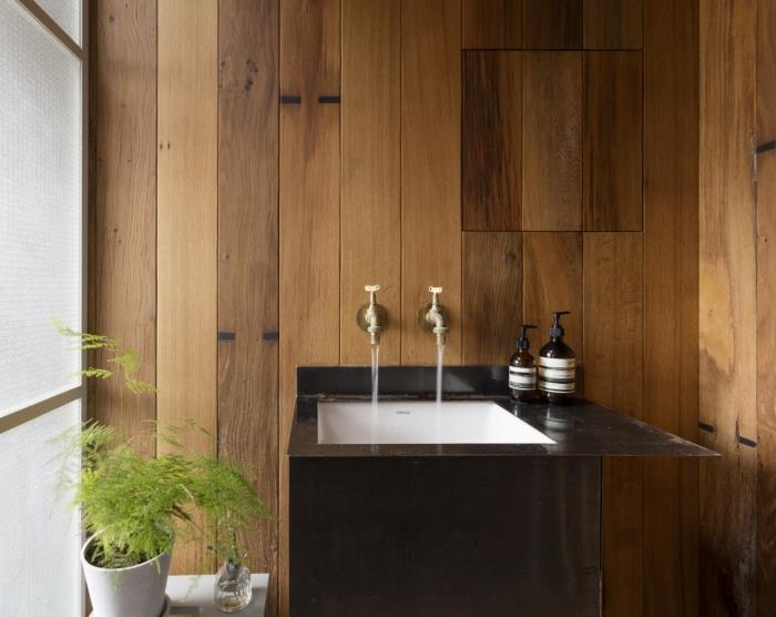 Japoniško stiliaus medinio vonios kambario dizainas, nedidelis vonios kambario apdaila su medinėmis sienomis su baltos ir juodos spalvos kriaukle