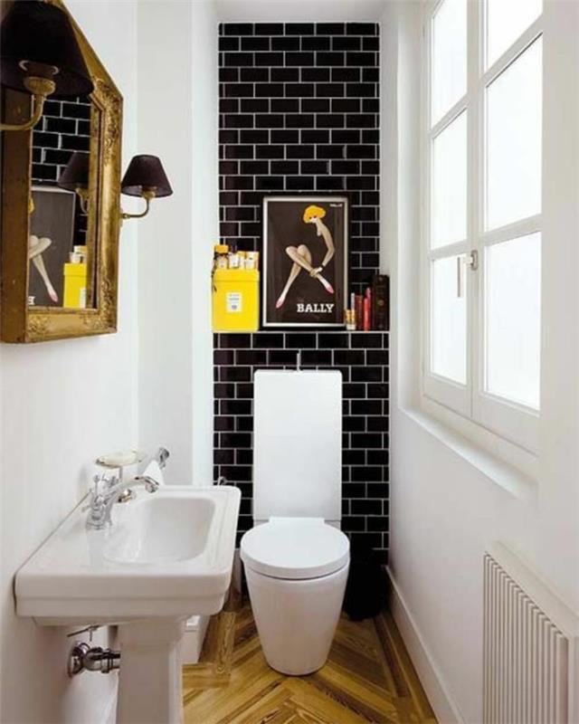 majhna kopalnica s črnimi opekami okoli stranišča in belimi stenami z velikim starinskim ogledalom z zlatim okvirjem