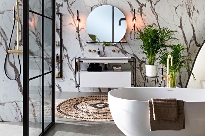 sodobna marmorna kopalnica s samostoječo kadjo s sodobnimi linijami in italijansko prho, omejeno z industrijsko stekleno streho, sodobna kopalnica z minimalističnim duhom in naravo, okrašena z zelenimi rastlinami in okroglo preprogo iz naravnih vlaken