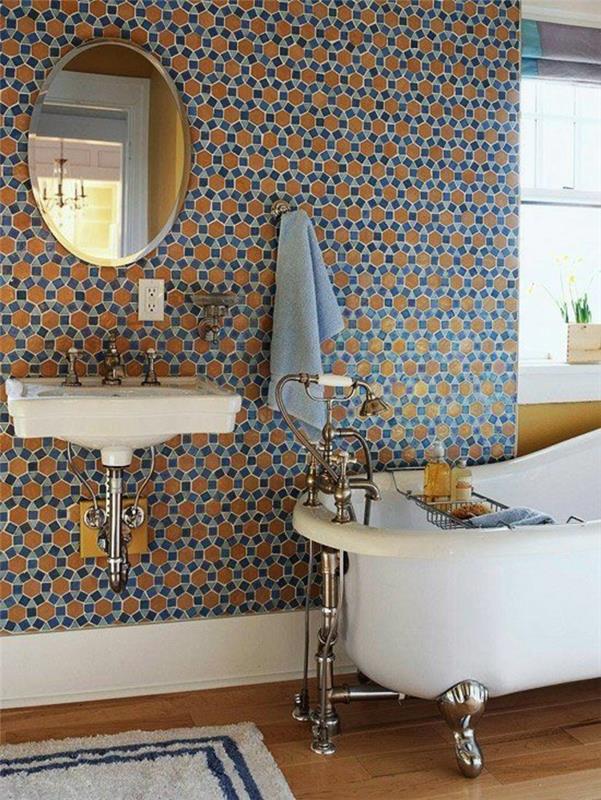 mažas vonios kambarys su mėlynomis ir oranžinėmis avilių sienomis su apvaliu veidrodžiu