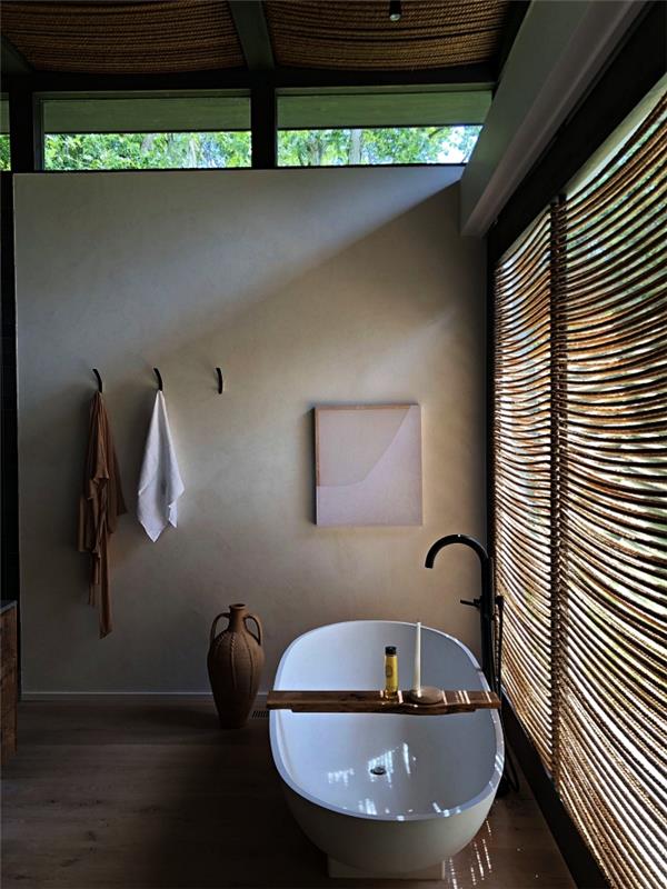 kopalnica v naravi in ​​zen z minimalističnim dizajnom s samostoječo kadjo in velikim oknom, ki omogoča vstop naravne svetlobe