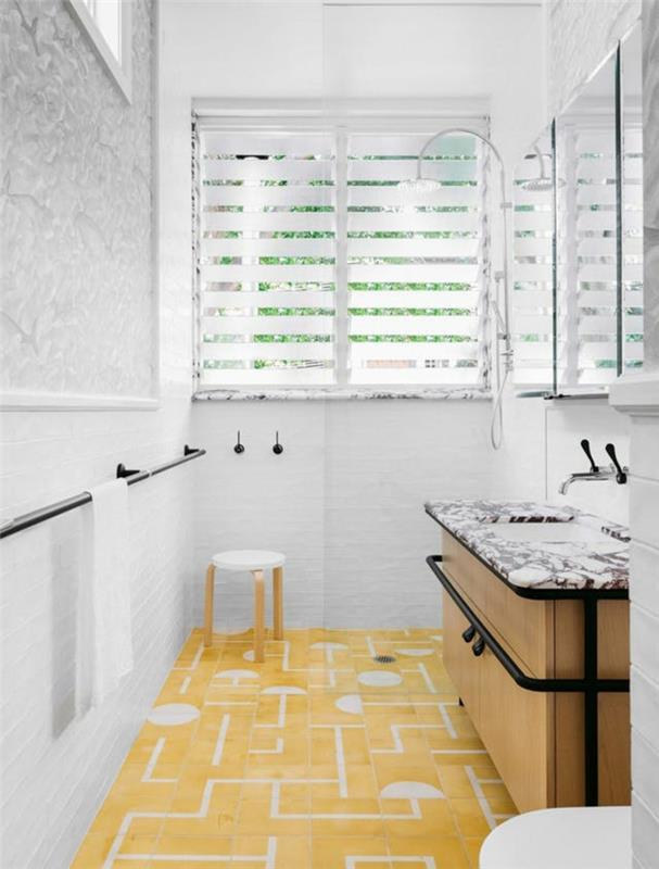 banyo için beyaz duvar dekorasyonu, grafik desenli sarı ve beyaz karo zemin, sarı meta ayaklı beyaz küçük yuvarlak tabure, siyah ve beyaz mermer imitasyon yüzeyli lavabo dolabı