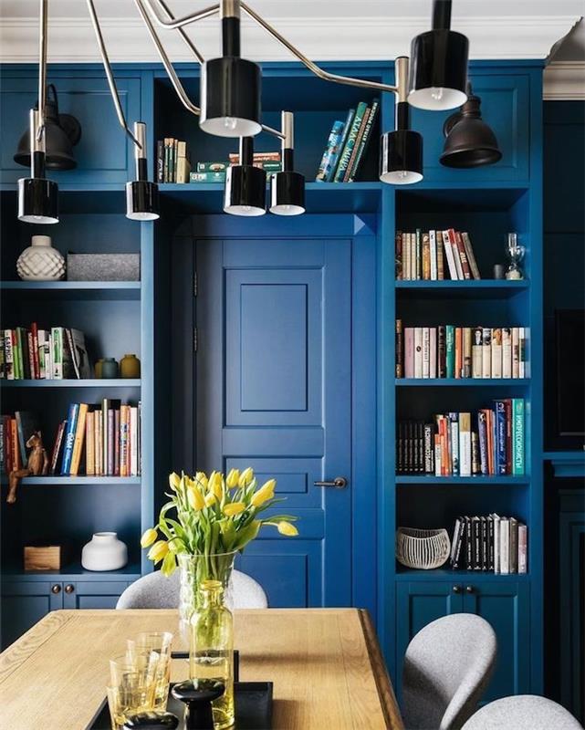 modre stene in vrata, majhna knjižna omara ob jedilnici z leseno mizo in sivimi stoli