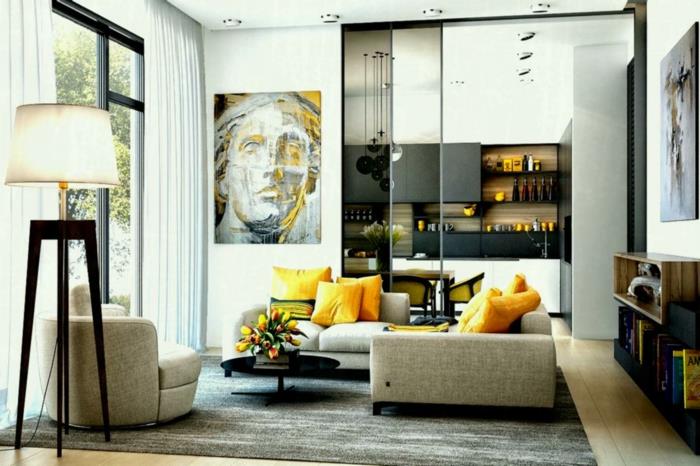 sodobna in sivo-bela dnevna soba, rumene blazine, umetniški portret, velika štirinožna svetilka, steklena streha delavnice s pogledom na kuhinjo