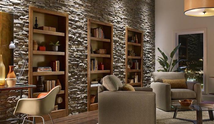 gyvenamojo kambario siena, padengta pilkomis akmenimis, supančiomis medines lentynas ir knygų spintas