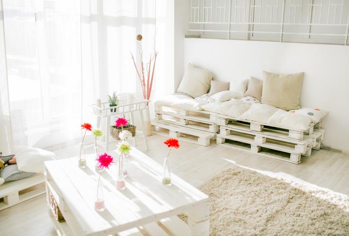 Beyaza boyanmış palet mobilyalarla donatılmış zarif ve rahat, tamamen beyaz oturma odası, çekyatla uyumlu palet sehpa