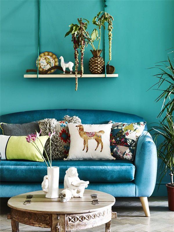 graži povo mėlyna aksominė sofa, paryškinta skirtingomis etninėmis pagalvėmis ir egzotišku dekoru