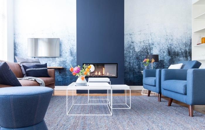 soğuk renkleri uyumlu bir şekilde birleştiren mavi ve beyaz oturma odası dekoru, bitişik duvarın grafik baskılı duvar kağıdıyla eşleşen lacivert boyalı şömine