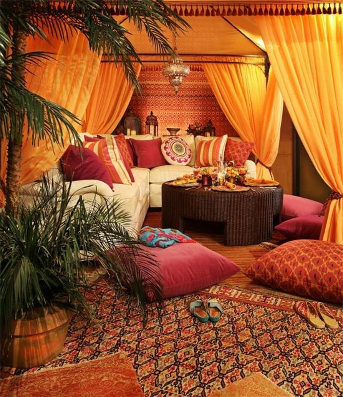bohemiškas dekoras, etniniai kilimai, dekoratyvinės pagalvėlės, apvalus stalas, ilgos oranžinės užuolaidos