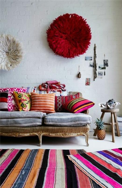 bohemiška apdaila, pilka sofa, įvairiaspalvis kilimas, medinis stalas, raudonas pufas