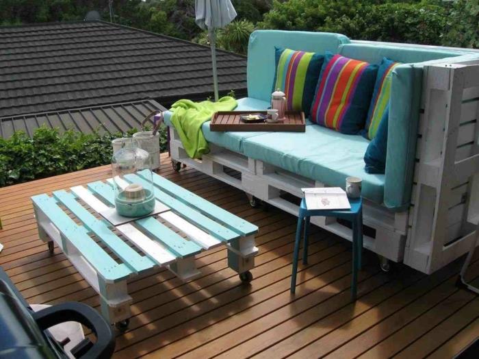 padėklų sodo stalas, padėklų fotelis, padėklų sofa, baldai padengti žaliu čiužiniu, etninių spalvų ir raštų pagalvėlės, pastelinės mėlynos spalvos plastikinė kėdė, pastelinės mėlynos ir baltos spalvos kavos staliukas su juodais ratukais