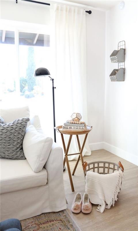svetainės zona balto skandinaviško stiliaus gyvenamajame kambaryje su balta sofa, papuošta pilkos tekstūros rašto pagalve, senovinio dizaino šoniniu stalu ir laikymo krepšeliu