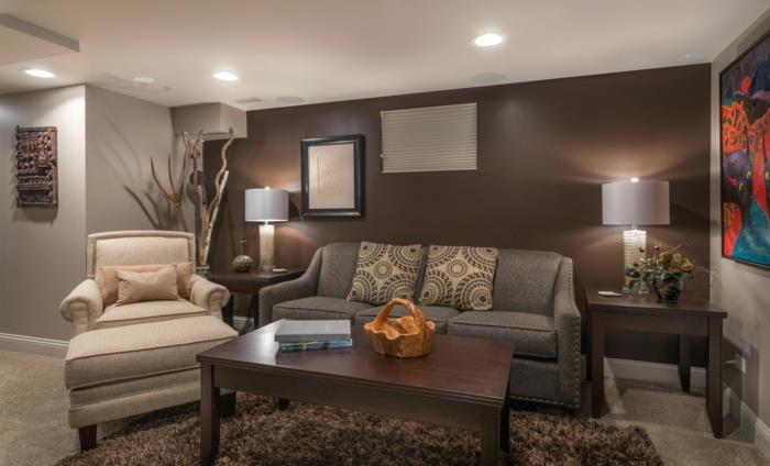 kreminis fotelis, rudas stalas, plaukuotas taupe kilimas, pilka sofa, taupe sienų dažai; abstrakti tapyba