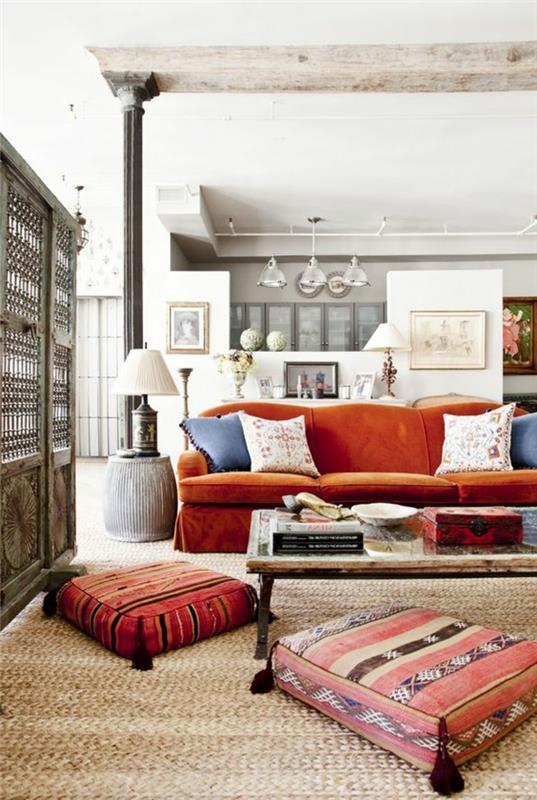 etninė svetainė, rytietiškos grindų pagalvėlės, oranžinė sofa, žalia mediena ir geležinis stalas