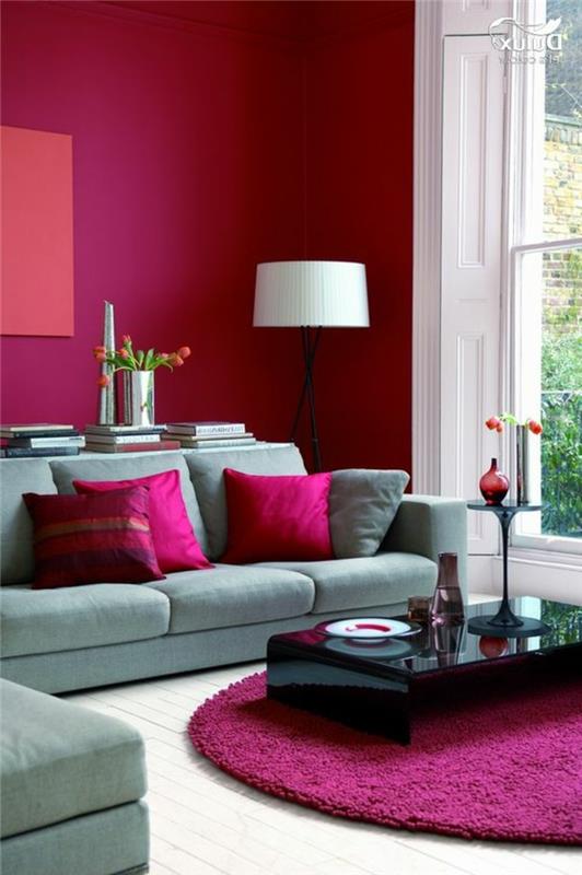 pilka ir rožinė svetainė, violetinis rožinis kilimas, juodas kavos staliukas, kampinė sofa, rausvos pagalvėlės